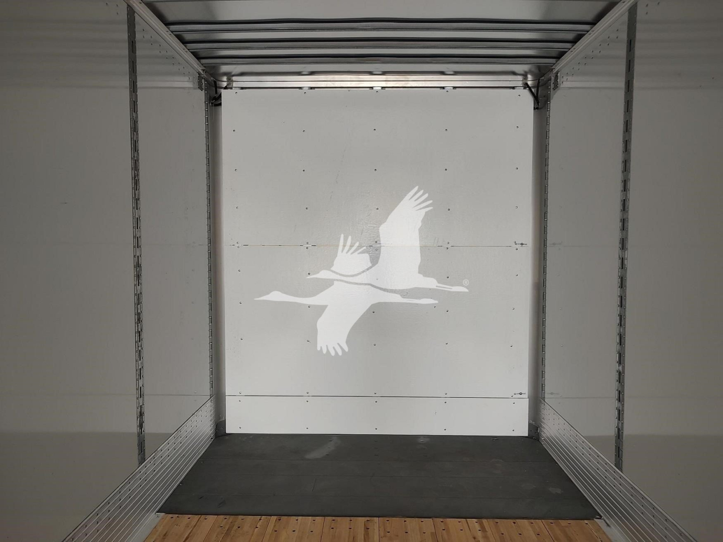 Interior of a Vanguard VXP trailer showing metal frame walls and a white rear door with a floating bird decal. Empty cargo space with a wooden floor strip.