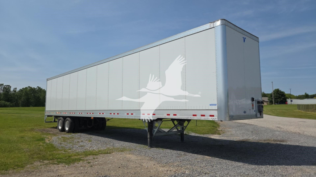 Trailer undercarriage and side view showing a Vanguard VXP box trailer on a gravel lot with a long gray body and tandem axles.