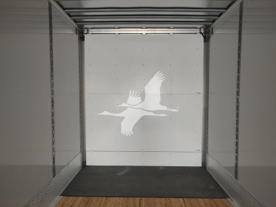 Interior of a Vanguard VXP trailer showing metal frame walls and a white rear door with a floating bird decal. Empty cargo space with a wooden floor strip.