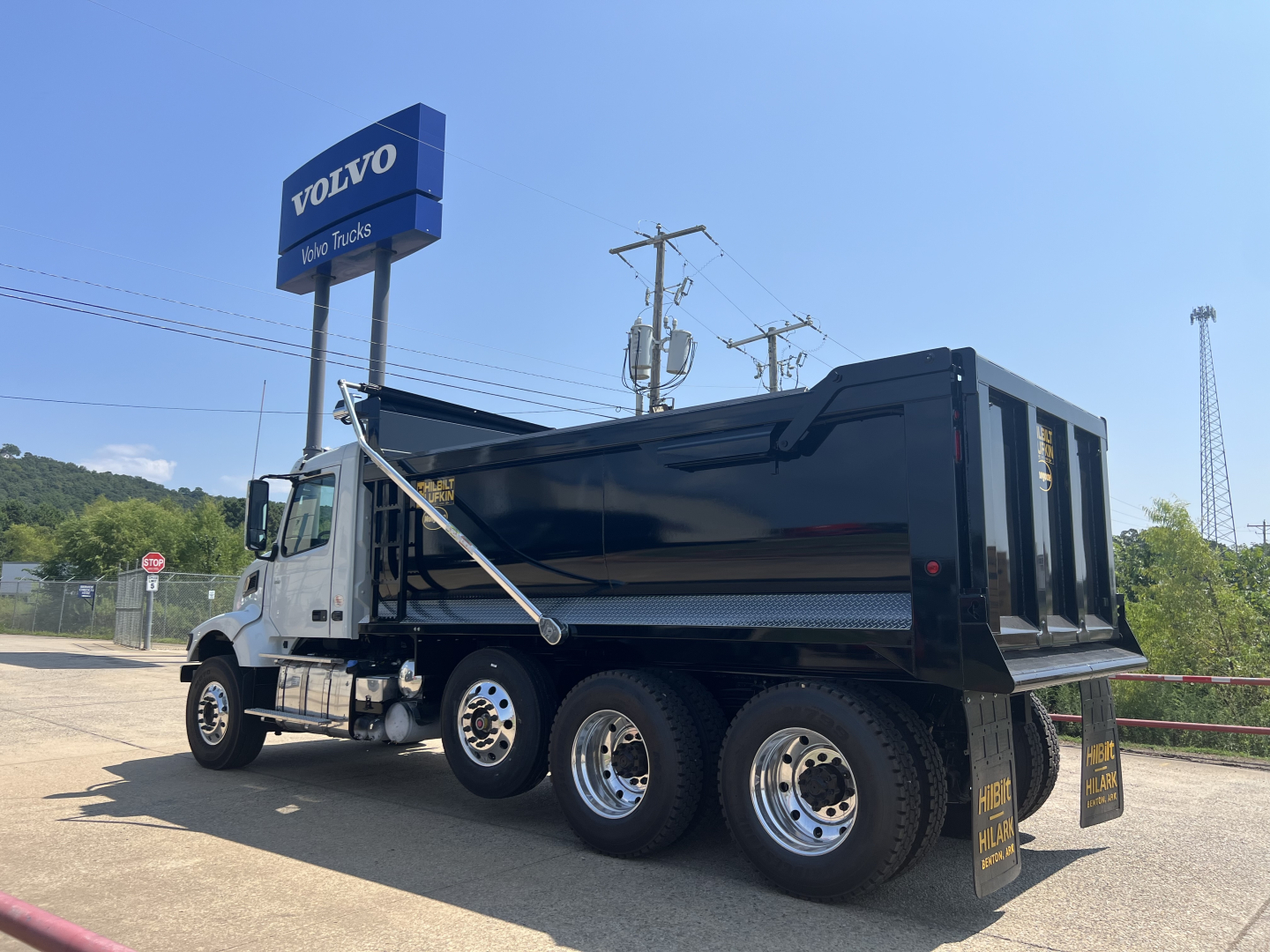 Dump truck showing a black Volvo VHD64F300 dump bed with chrome wheels and white cab, side view.