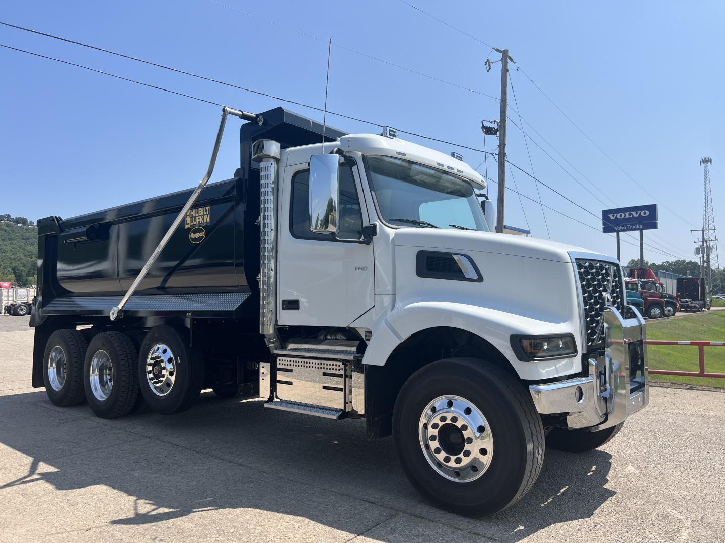 Volvo VHD64F300 dump truck in showroom view showing cab, chrome grille, large side mirrors, and black dump bed with Volvo logo.