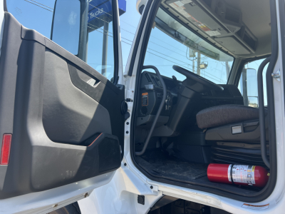 Cab interior of a Volvo VHD64F300 dump truck showing open driver door, steering wheel, dashboard, and a fire extinguisher on the floor.
