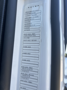 Volvo label on door jamb showing vehicle identification details and axle configuration for a Volvo VHD64F300 dump truck.