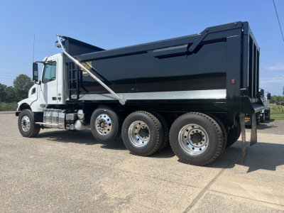 Dump truck in profile view showing black dump body, white cab, chrome steps, and multiple axles (three rear).