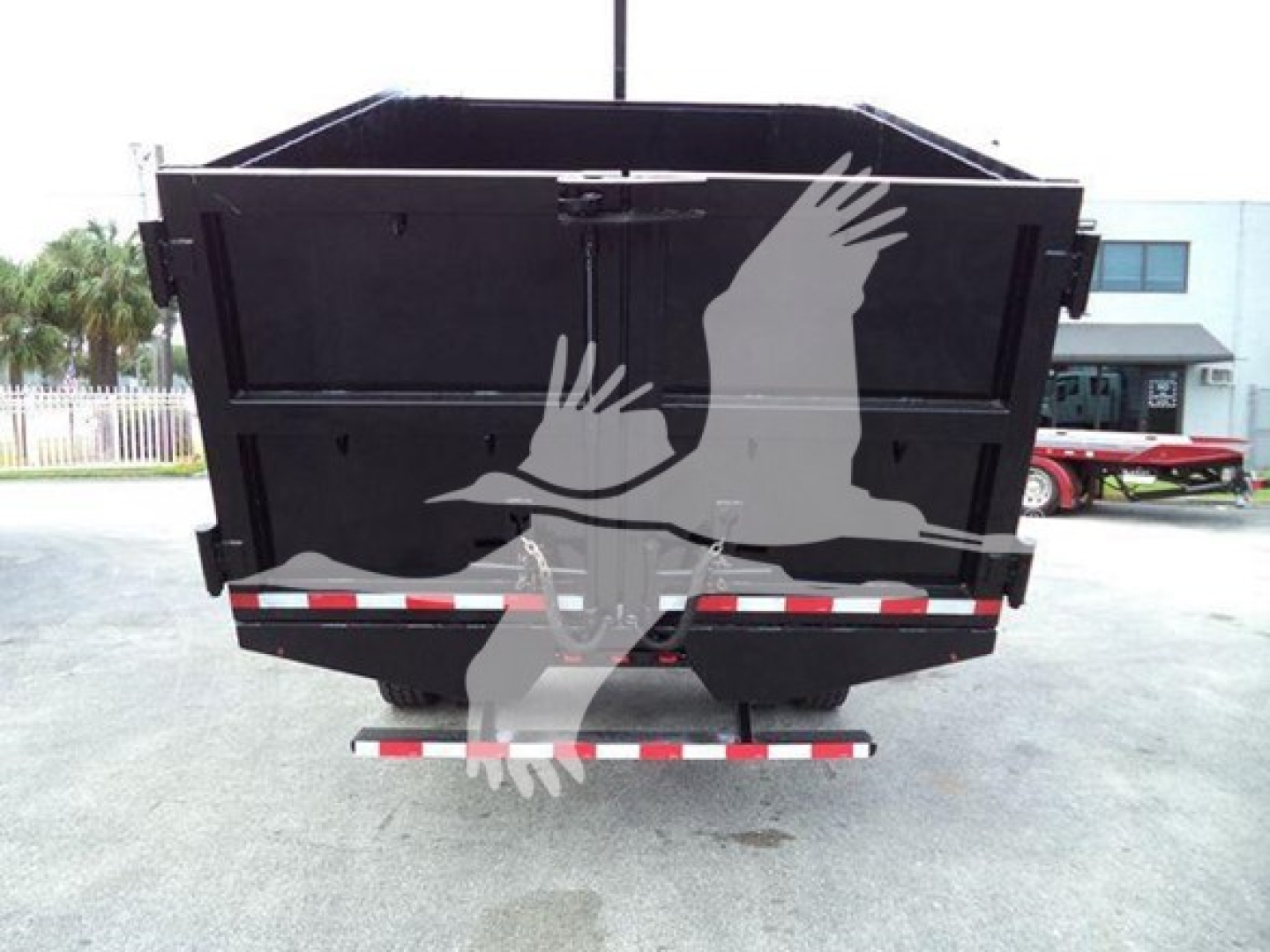 Rear view of a black dump body trailer on a Peterbilt 337 with chain bars and reflective tape. No legible model text visible.