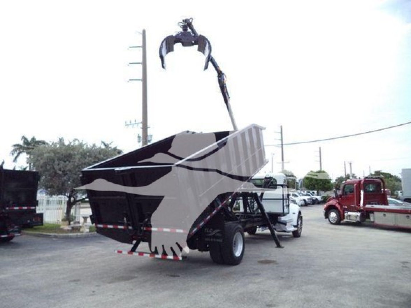 Truck chassis showing a grapple truck with a large dump bed and hydraulic grapple arm in a yard.