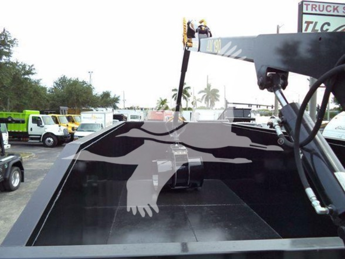 Peterbilt 337 grapple truck bed with hydraulic machinery and controls visible; cab not in frame; trucks and equipment in background.