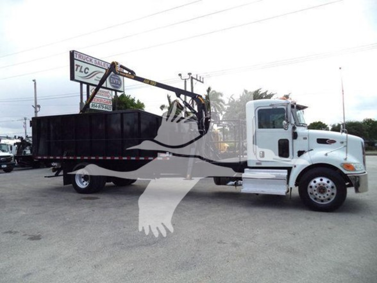 Peterbilt 337 grapple truck side view with crane arm and flatbed in a dealership lot.