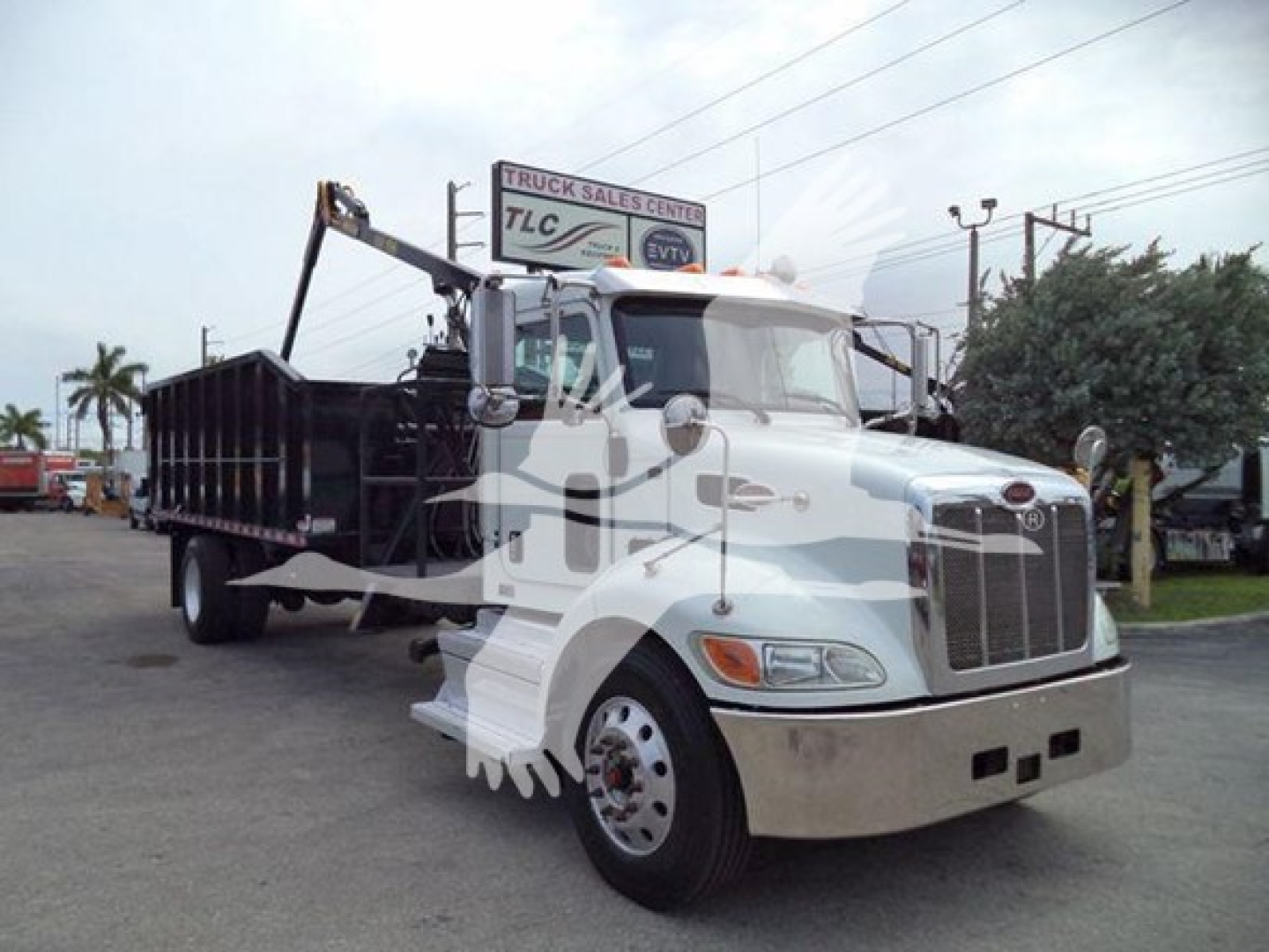 Peterbilt 337 dump truck with grapple body, white cab, front grille, dual mirrors, and crane arm on a dealership lot.