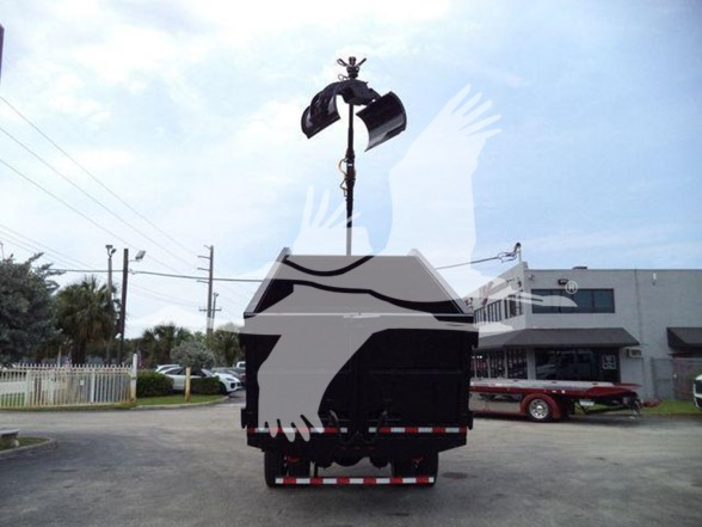 Back view of a 2020 Peterbilt 337 grapple truck being loaded or unloaded with a crane hook in a truck yard.