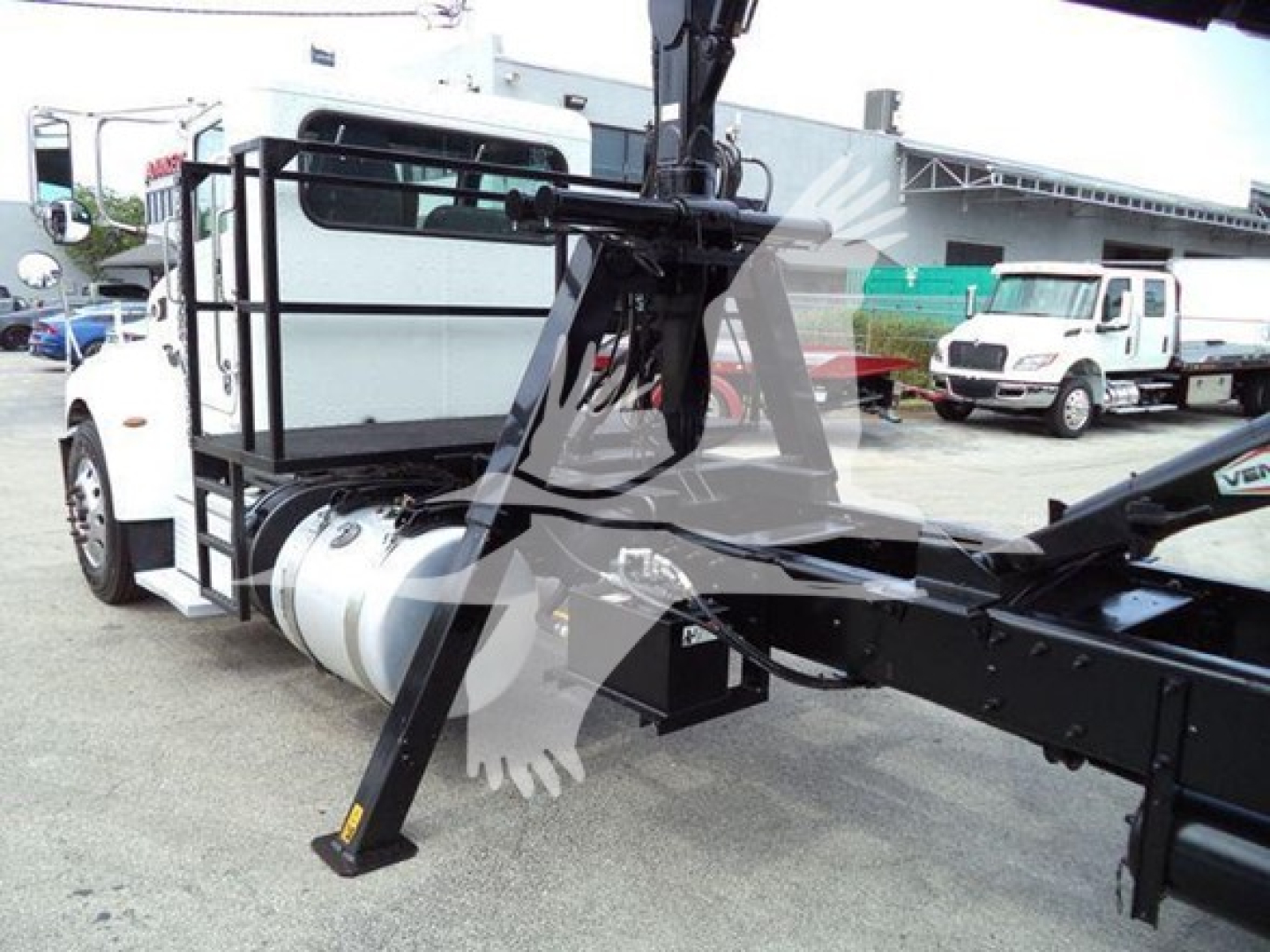 Peterbilt 337 truck chassis with grapple arm attachment and auxiliary lifting mechanism, side view showing cab, fuel tank, and framework.