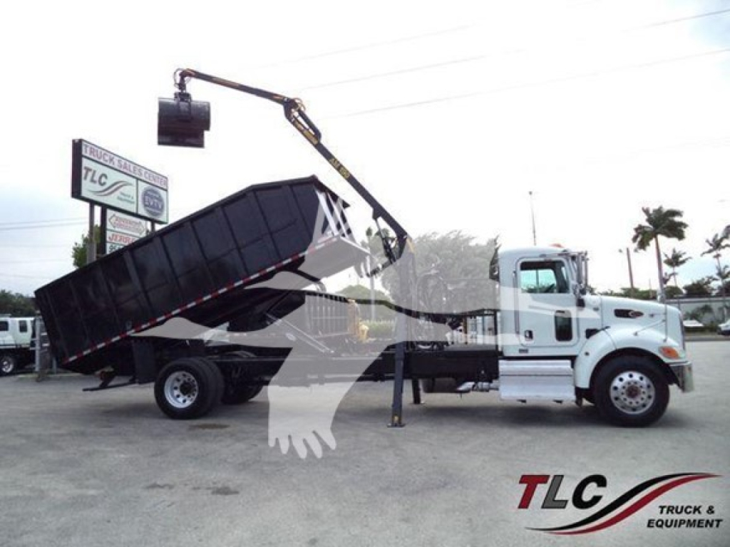Truck cab with a grapple truck bed and hydraulic crane in operation, 2020 Peterbilt 337, side view showing a large dumping hopper elevated by a crane.