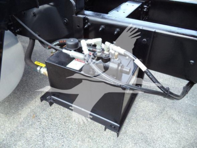 Grapple truck engine bay area showing hydraulic reservoir and hoses mounted in a black metal box under the chassis.