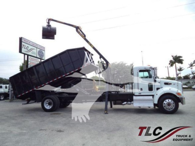 Truck cab with a grapple truck bed and hydraulic crane in operation, 2020 Peterbilt 337, side view showing a large dumping hopper elevated by a crane.