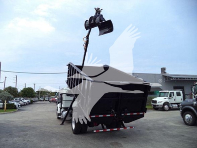 Peterbilt 337 grapple truck with crane grapple raised, in a dealership lot, rear view showing dump bed and hitch area.