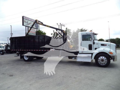 Peterbilt 337 grapple truck side view with crane arm and flatbed in a dealership lot.