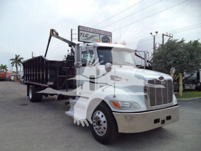 Peterbilt 337 dump truck with grapple body, white cab, front grille, dual mirrors, and crane arm on a dealership lot.