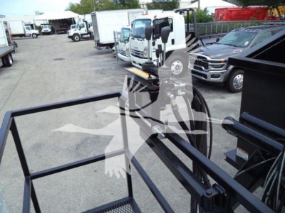 Peterbilt 337 grapple truck in a used inventory lot with a metal grapple frame in foreground and other trucks in background.