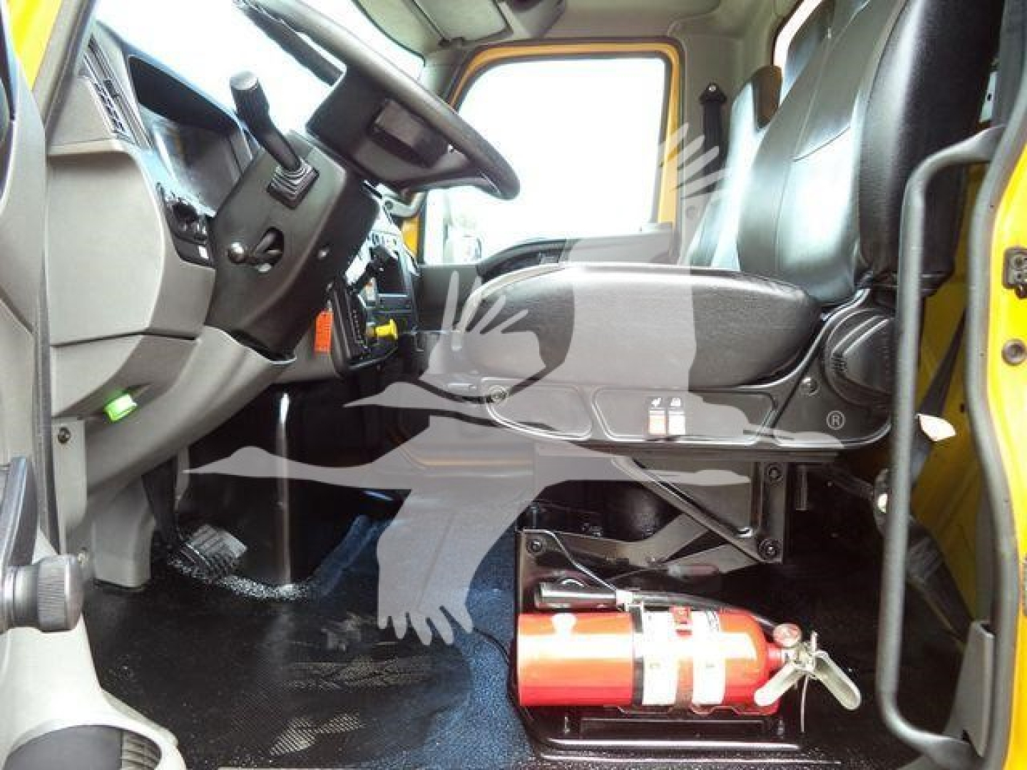 Truck cab interior of a 2020 International MV, driver seat and steering wheel visible with fire extinguisher mounted under the seat area.