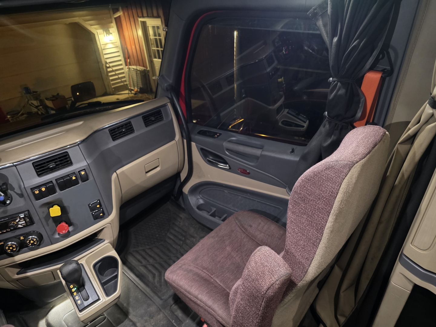 Peterbilt 579 cab interior view with driver seat, dashboard controls, and steering wheel.