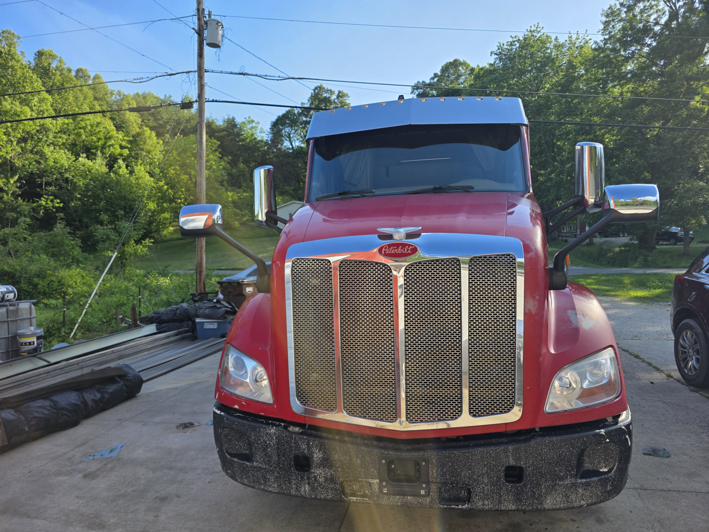 Peterbilt 579 truck front view showing large chrome grille and red cab, side mirrors, and bumper.