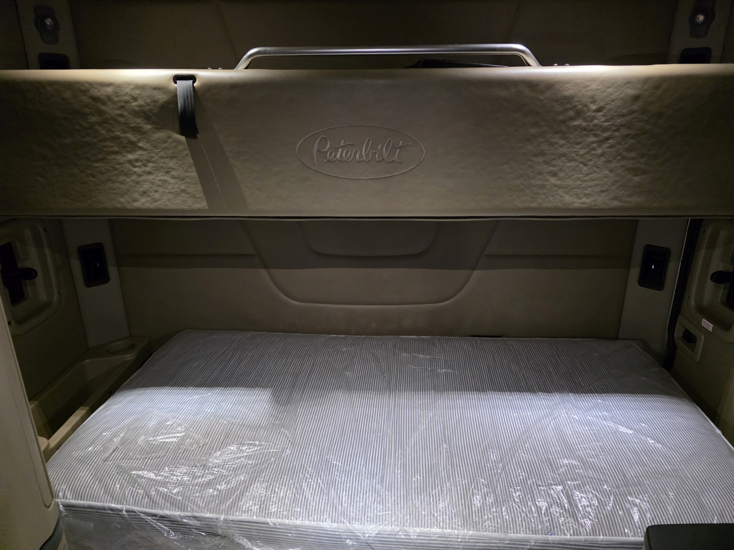 Peterbilt 579 sleeper cab rear interior showing overhead bunk area and plastic-wrapped bed.