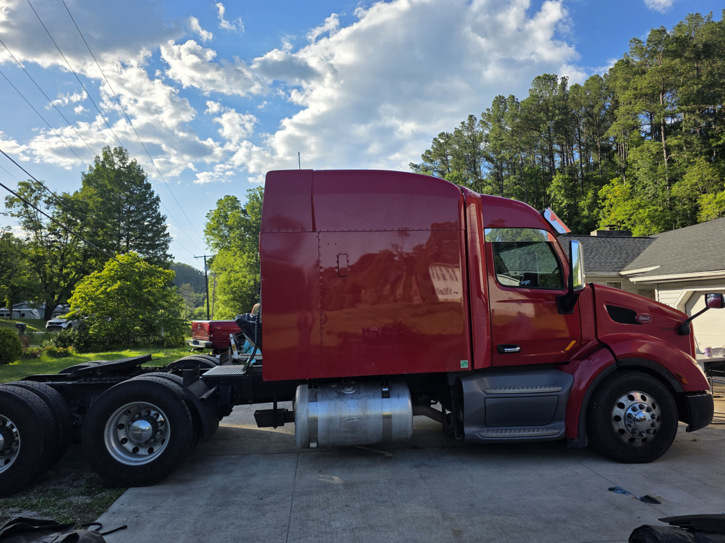 Truck side view of a red 2016 Peterbilt 579 conventional sleeper tractor with a long hood and dual rear axles exposed.