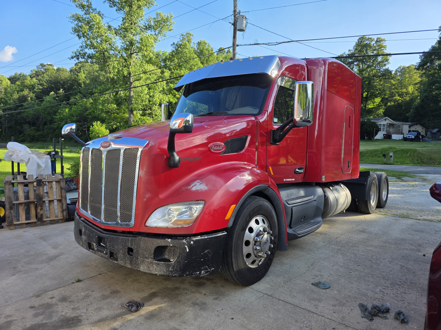 Peterbilt 579 truck in red with sleeper cab, front view, diesel exhaust, daytime outdoor lot.