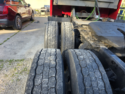 Peterbilt 579 truck chassis with three rear axles visible; wear on tire tread and road grime on components.