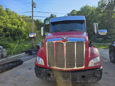 Peterbilt 579 truck front view showing large chrome grille and red cab, side mirrors, and bumper.