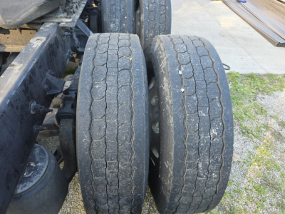 Tractor trailer dual rear tires along chassis showing tread wear and asphalt edges.