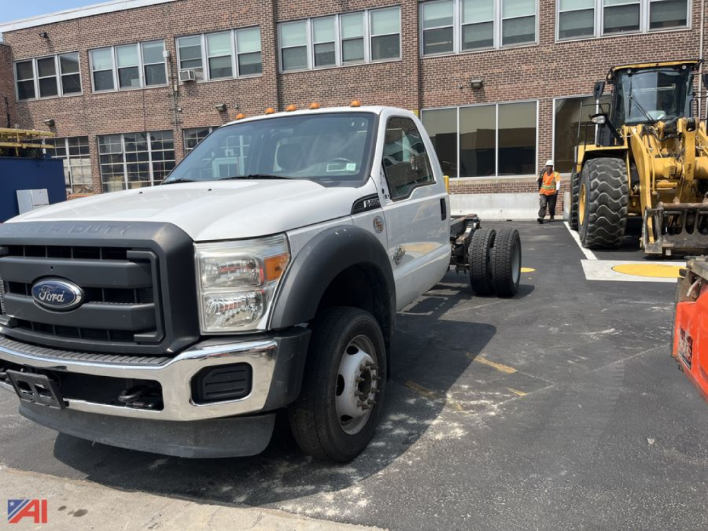 Ford F-550 cab and chassis in a parking lot, front-left view, with dual rear wheels and a large construction vehicle in the background.