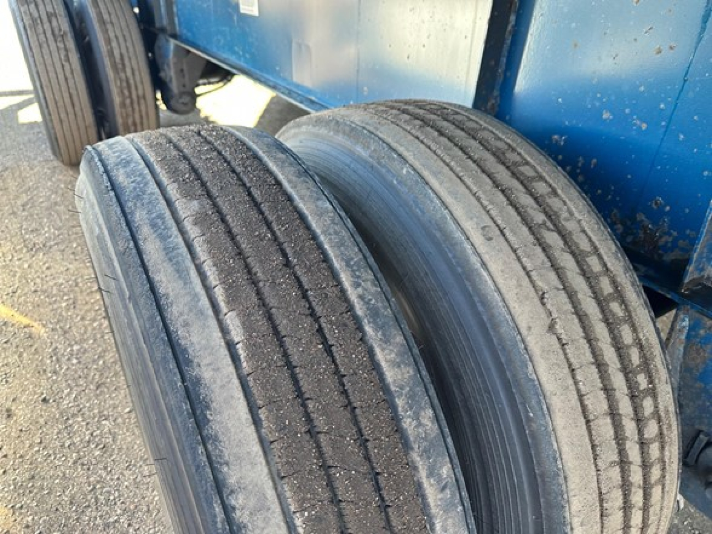 Trailer tires visible beneath a blue Great Dane flatbed trailer showing treaded dual wheels and wheel wells.