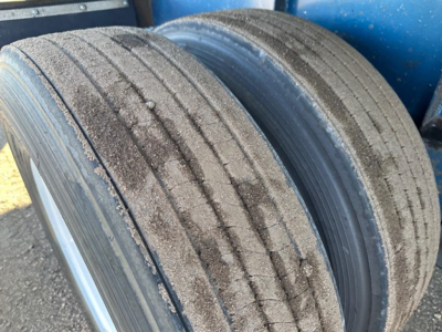 Great Dane flatbed trailer wheel and tire close-up showing worn tread and dirt buildup on dual rear axles.