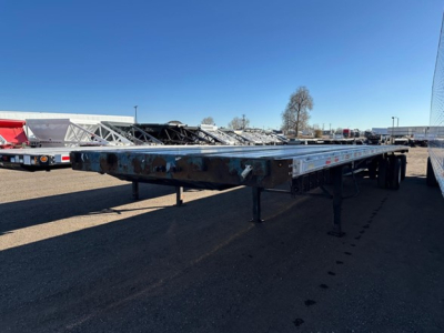 Flatbed trailer from a Great Dane Freedom LT model in a lot, showing the long chassis with adjustable legs and dual rear axles.