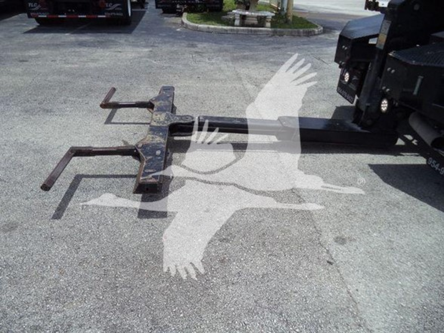 Winch hitch assembly with two long forks and mounting bar, on pavement next to a Ram truck, visible in a used-truck lot.