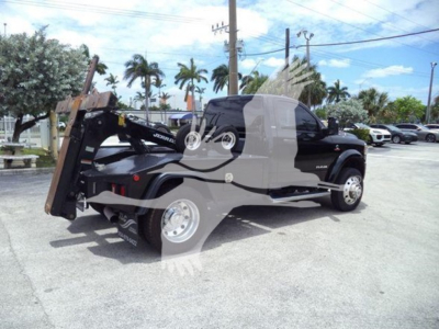 Ram 4500 pickup with hydraulic tilt bed and winch attachment visible; front view of chassis, tires, and palms in background.