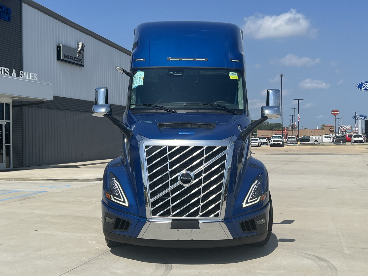 Volvo VNL64T860 truck front view showing chrome grille, headlights, and blue cab in sales lot.