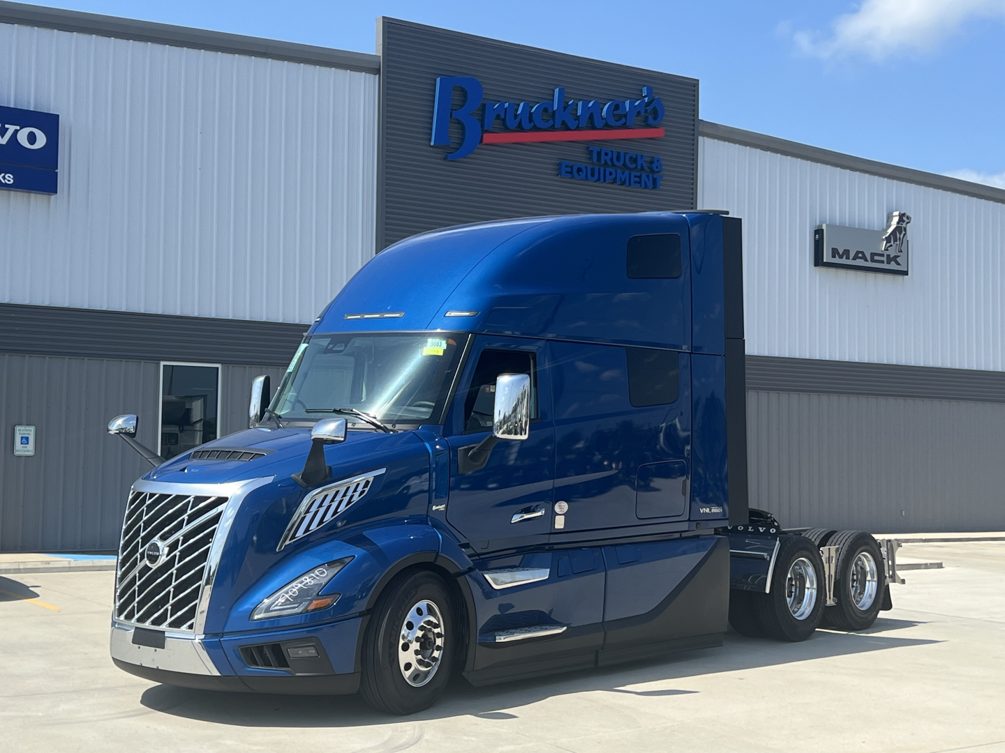 New Volvo VNL64T860 conventional sleeper tractor in blue parked outside a truck dealership with Brackeners Truck Equipment signage.