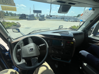 Volvo VNL cab interior showing steering wheel and dashboard in view, with large touchscreen display and center console; windshield shows exterior truck lot.