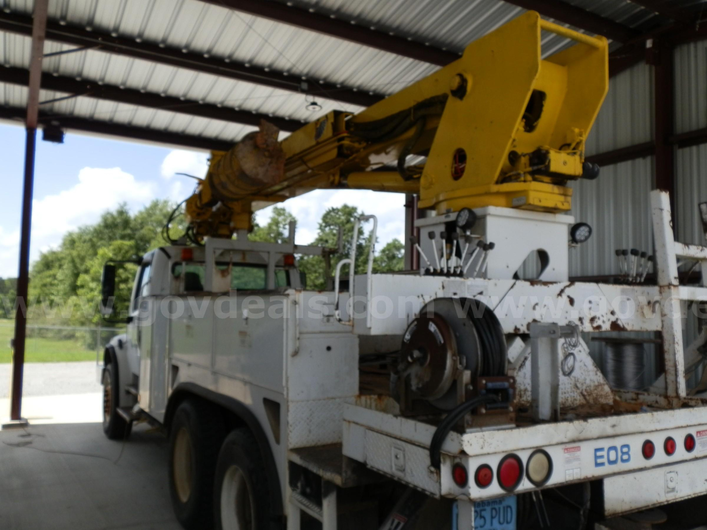 Service/utility truck chassis showing a large yellow freightliner boom in a covered area.