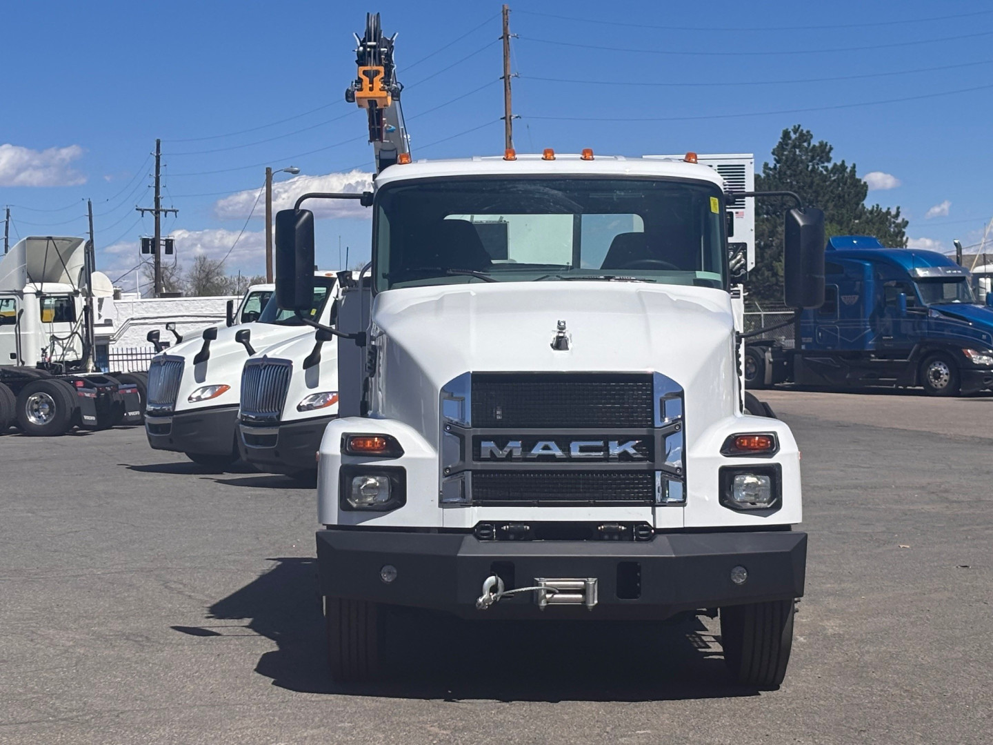 Front view of a white 2026 Mack MD7 truck with black grille, large bumper, and visible winch hook in a dealership lot.