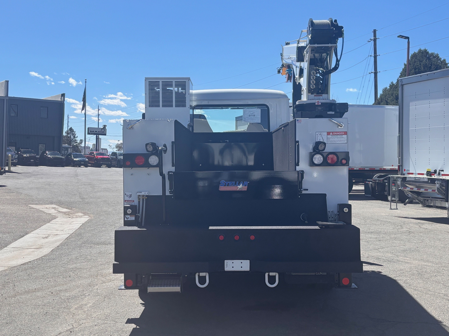 Truck rear view showing crane/boom equipment and tailboard with lights and hooks.