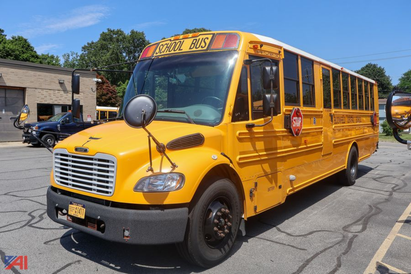 School bus front-left view showing bright yellow Freightliner Thomas C2 Saf-T-Liner with STOP sign and SCHOOL BUS sign on roof