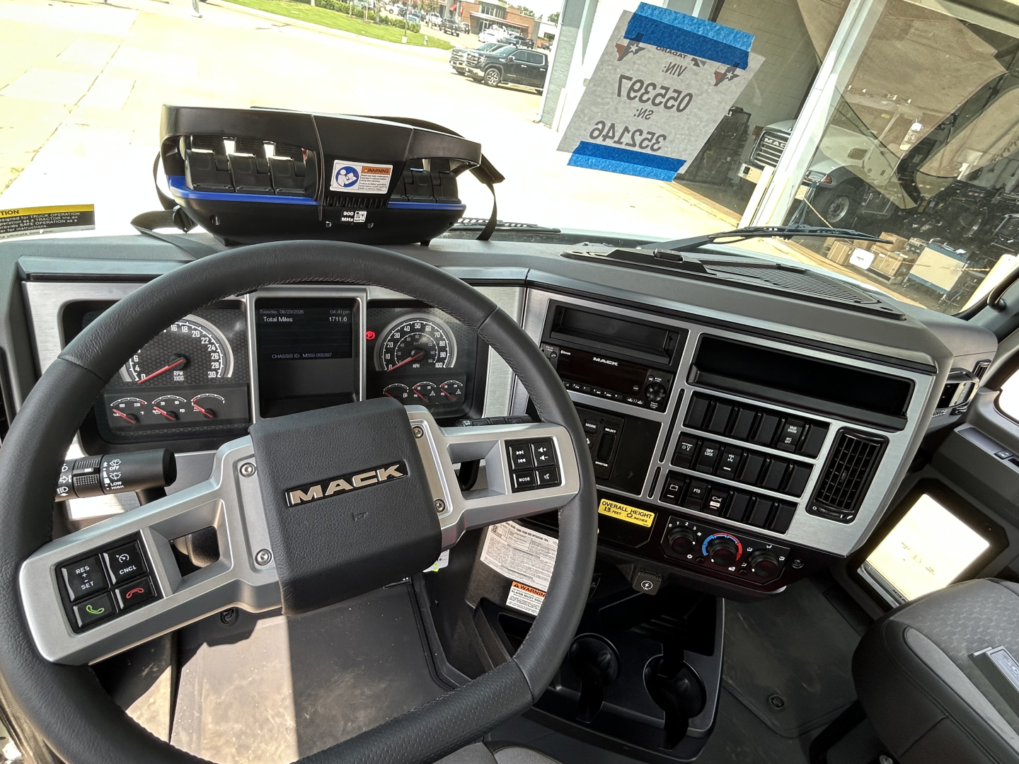 Cab interior of a Mack GR64F truck showing steering wheel with Mack logo, instrument cluster, center console, and dashboard controls.