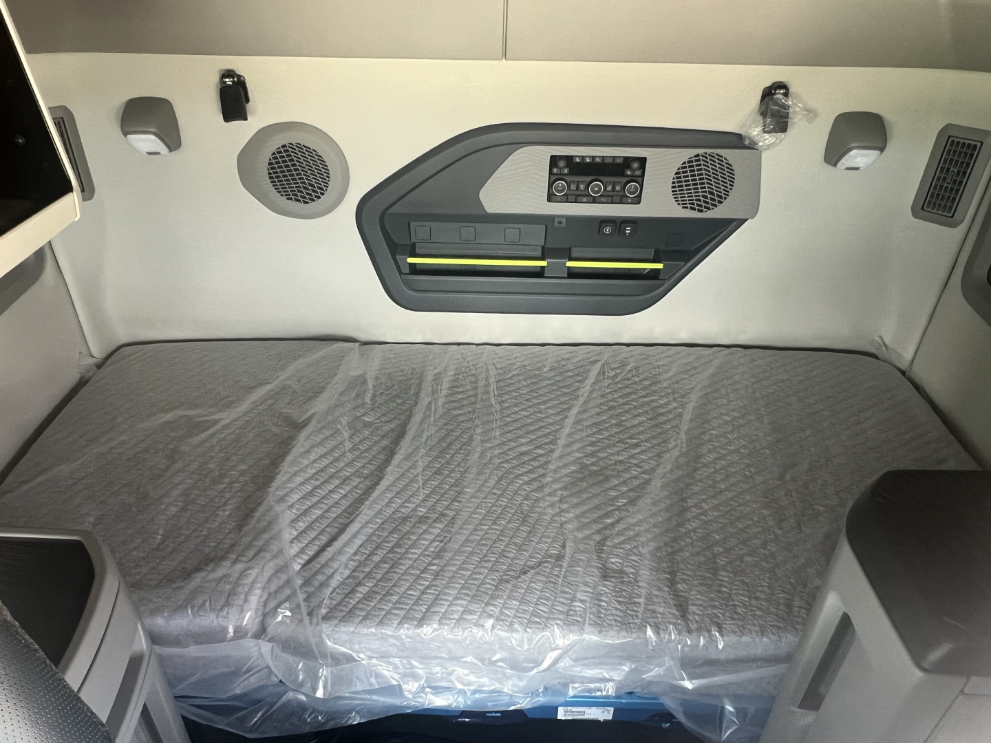 Volvo VNL64T660 truck sleeping compartment with control panel and storage net; printed labels or badges on the wall; plastic-wrapped mattress. 