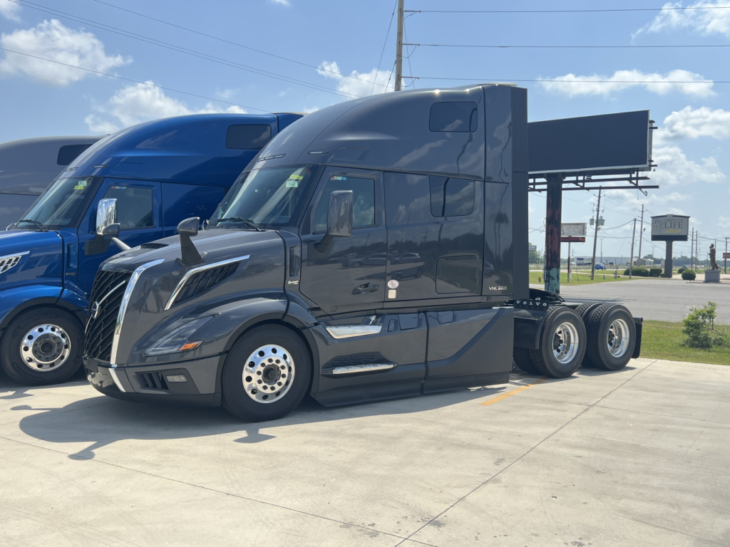 Volvo VNL64T660 sleeper cab tractor in service bay showing side profile and empty dump bed trailer connection.