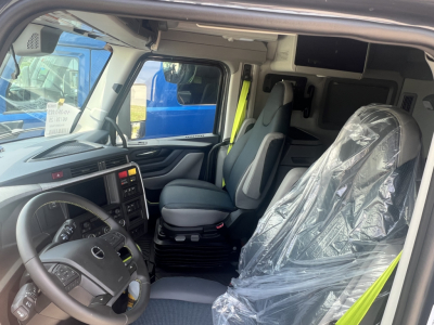 Volvo VNL truck cab interior showing steering wheel, dashboard, driver seat with plastic cover, and passenger seat. Visible text includes none legible from image apart from standard controls.