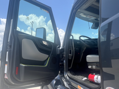 Volvo VNL64T660 cab interior with open driver door showing steering wheel and dashboard; exterior mirror and blue sky reflected; red fire extinguisher visible near door.