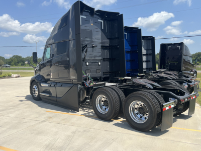 Truck tractor side view showing sleeper cab and dual rear axles with chrome wheels and black paint.